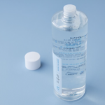 A clear, cylindrical bottle of calming toner with a white screw cap placed beside it on a light blue background. The toner bottle has blue and white text printed on it.